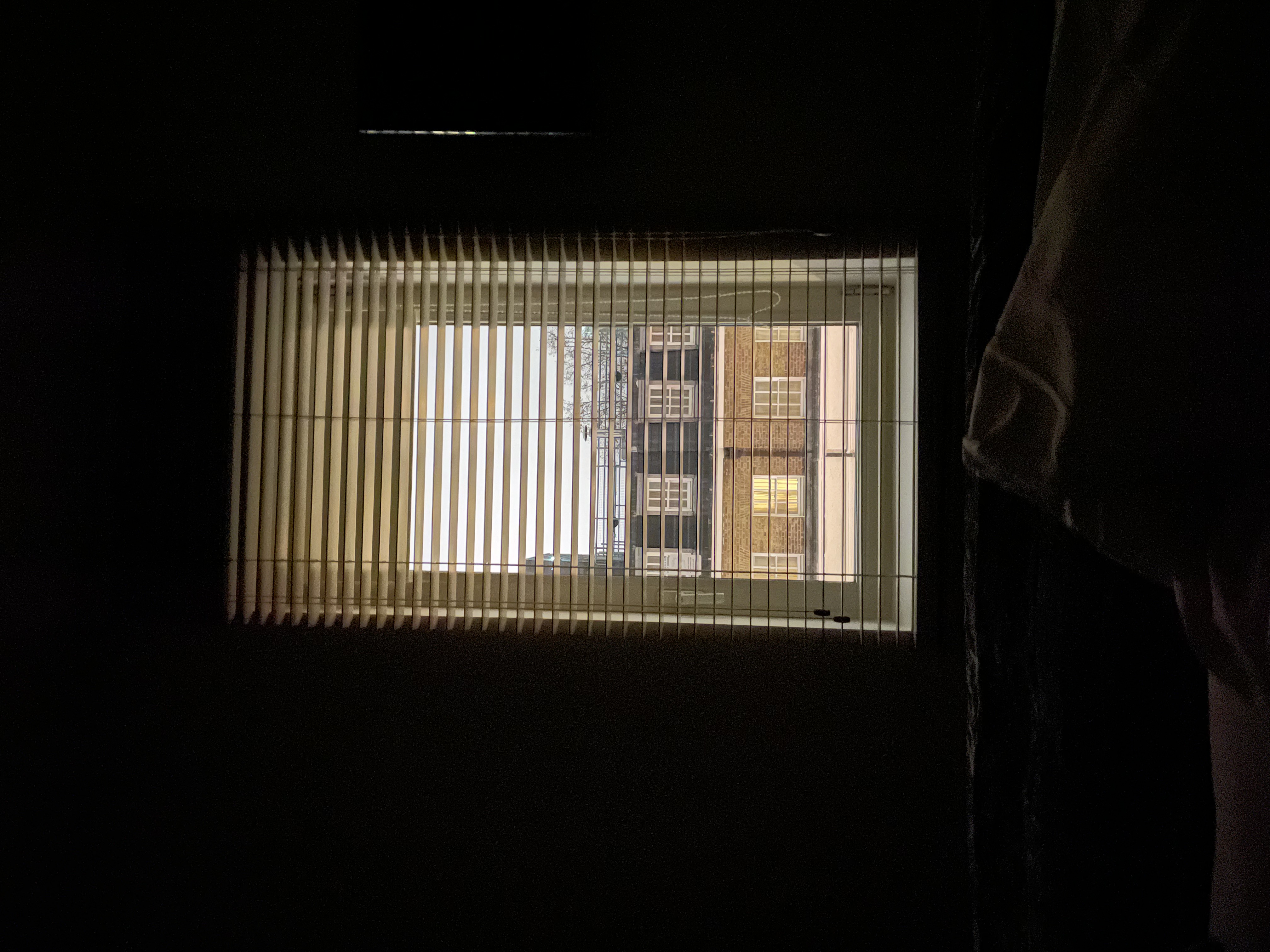 Dark room interior with venetian blinds, London Victorian brick facade outside